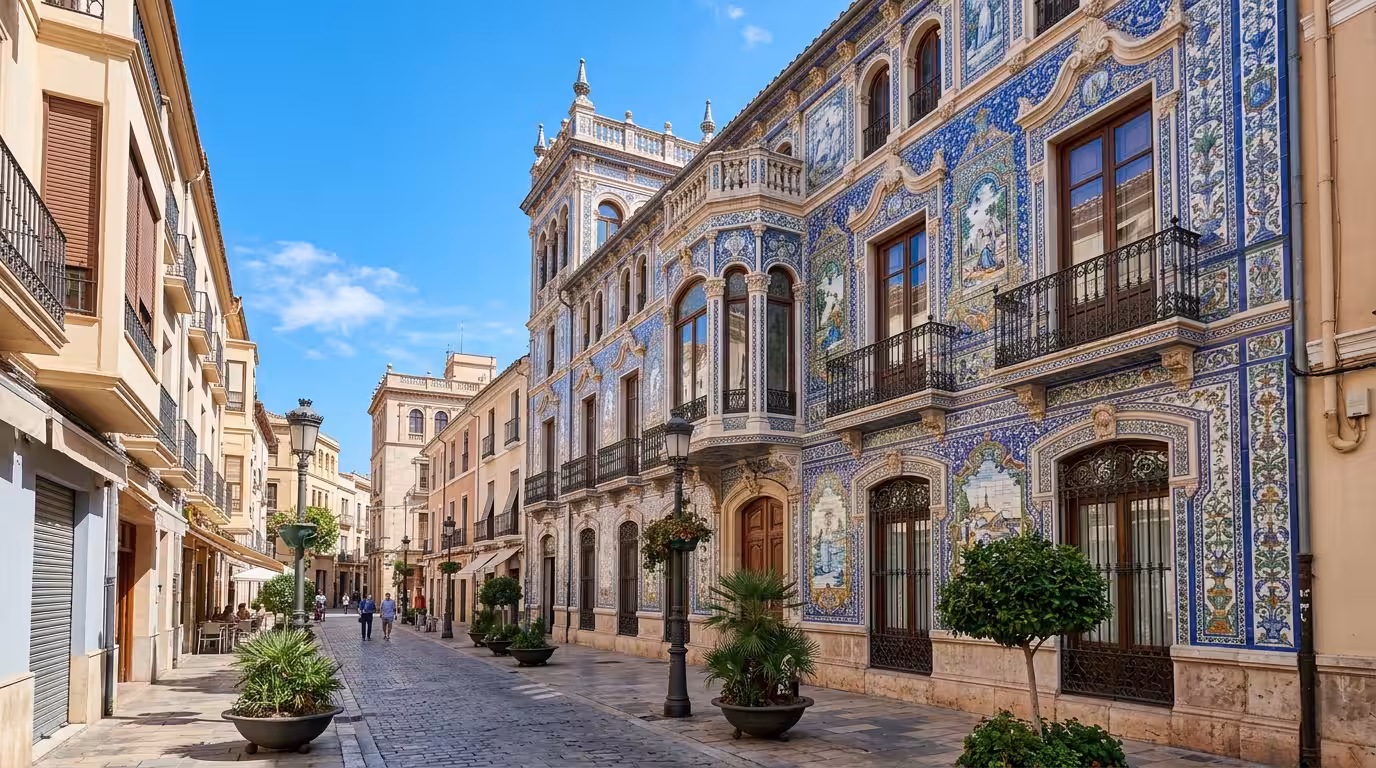 A wide cinematic shot of the historic city center of Castellón de la Plana on a bright midday, showing a grand modernist building facade covered in intricate hand-painted ceramic tiles in cobalt blue