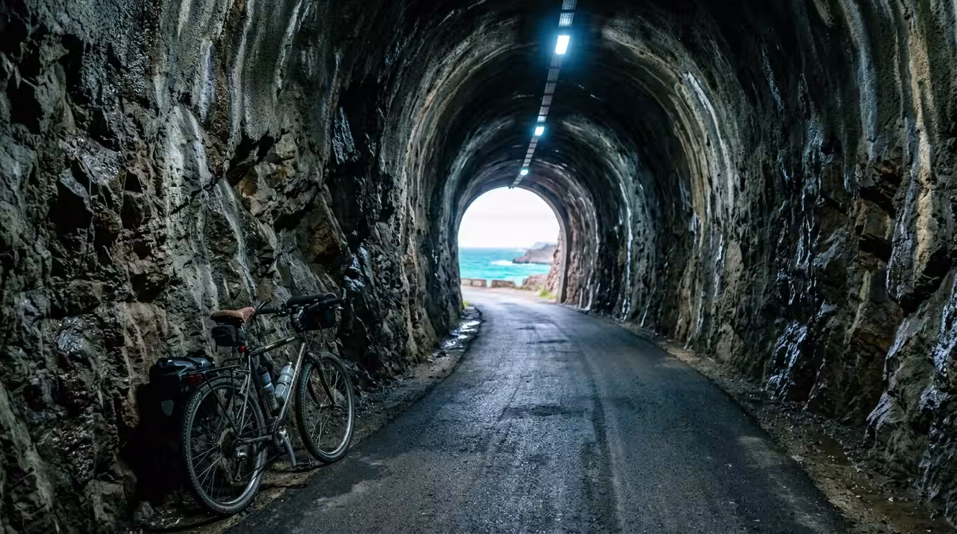 A documentary-style photograph taken inside the 600-meter tunnel of the Vía Verde del Mar in Castellón, Spain, looking toward the circular light at the tunnel exit where the Mediterranean Sea is faint