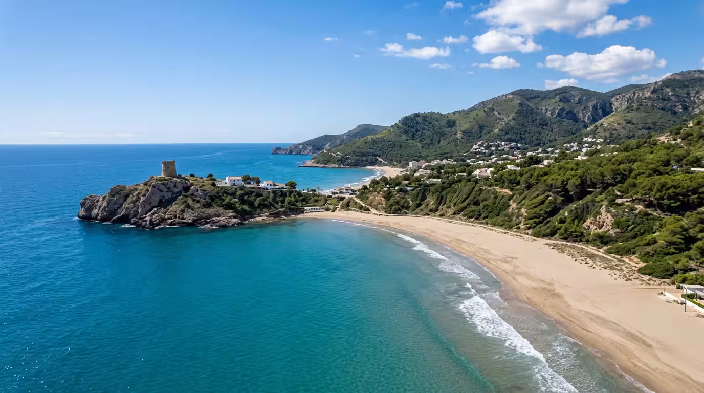 A wide cinematic aerial view of the Oropesa del Mar coastline in clear midday light, showing the curved sandy beach of La Concha, the rocky promontory with a medieval watchtower silhouetted against a 