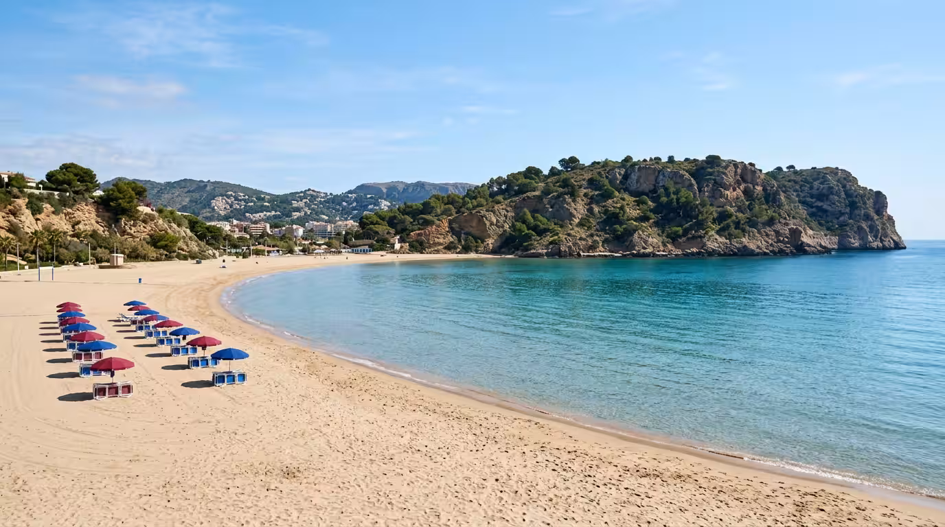 Paisaje costero de la playa de La Concha en Oropesa del Mar a primera hora de la tarde, con arena dorada limpia, mar turquesa sin oleaje, algunas sombrillas de tonos rojos y azules alineadas y acantil