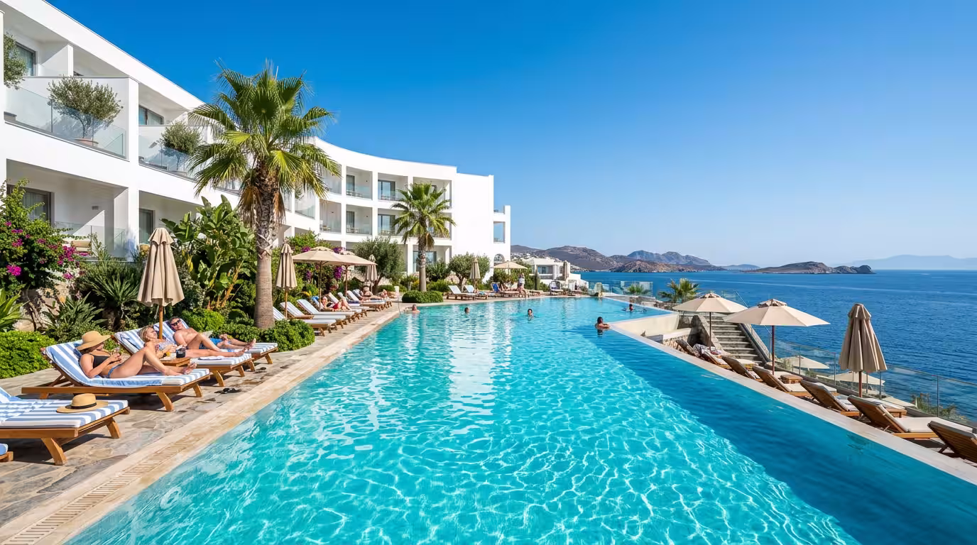 A luxurious Mediterranean hotel pool area at midday, with crystal-clear blue water reflecting the white facade of a modern resort building, surrounded by tropical palm trees and sun loungers, the sea